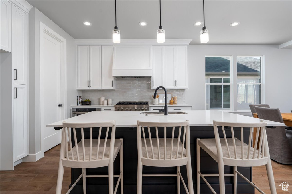 Kitchen featuring dark hardwood / wood-style flooring, custom range hood, decorative light fixtures, stove, and white cabinets