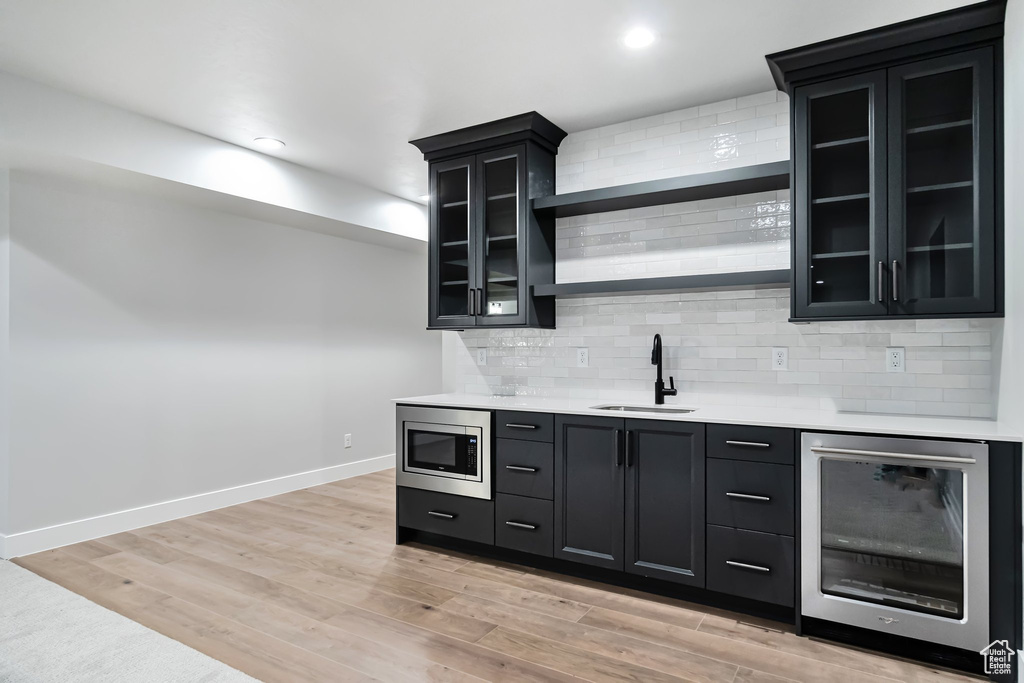 Kitchen featuring light hardwood / wood-style floors, tasteful backsplash, wine cooler, sink, and stainless steel microwave