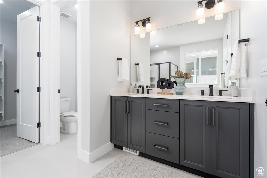 Bathroom with tile flooring, vanity with extensive cabinet space, dual sinks, and toilet