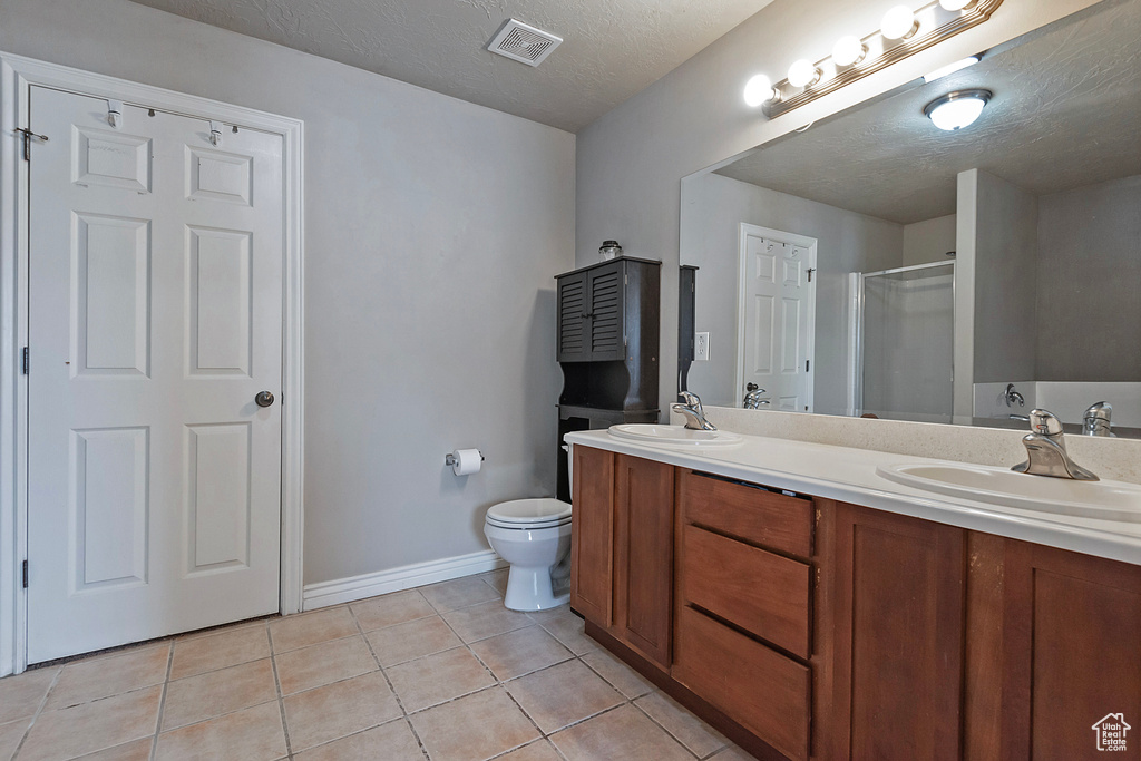 Bathroom with a textured ceiling, double sink vanity, toilet, and tile flooring
