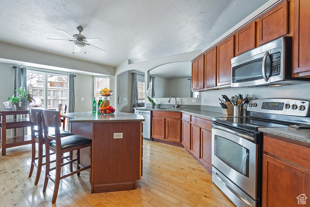 Kitchen featuring light hardwood / wood-style floors, appliances with stainless steel finishes, ceiling fan, a healthy amount of sunlight, and a kitchen island