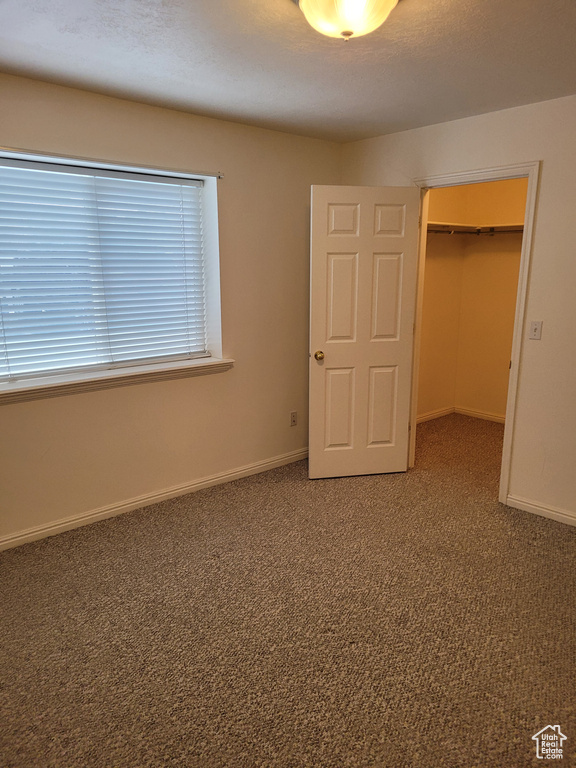 Unfurnished bedroom with a closet, a walk in closet, and dark colored carpet