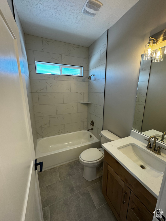 Full bathroom with tile floors, tiled shower / bath combo, toilet, and a textured ceiling