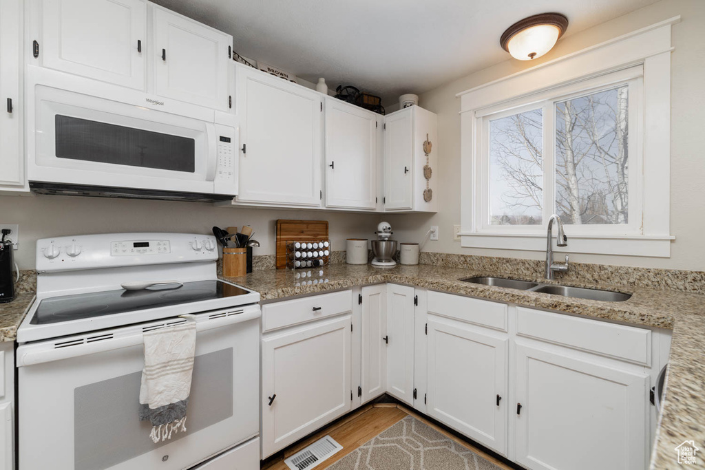 Kitchen featuring light hardwood / wood-style floors, white cabinetry, stone countertops, white appliances, and sink