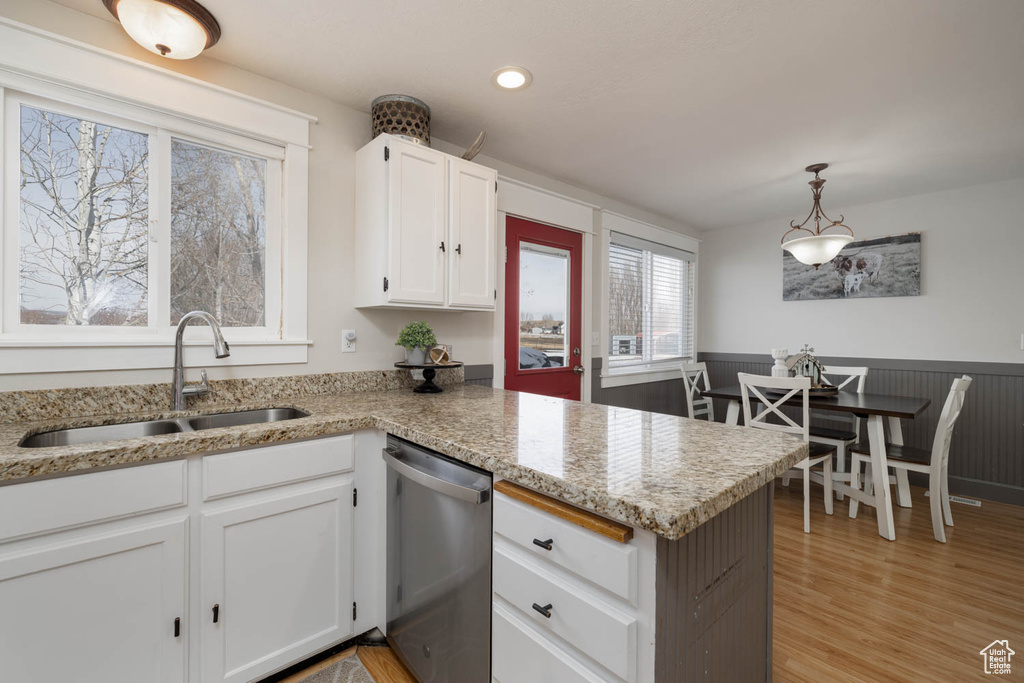 Kitchen featuring hanging light fixtures, white cabinets, light hardwood / wood-style flooring, stainless steel dishwasher, and sink