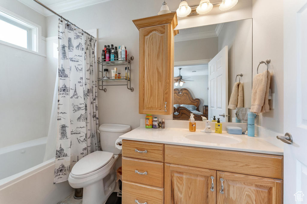 Full bathroom with ornamental molding, toilet, vanity with extensive cabinet space, ceiling fan, and shower / tub combo