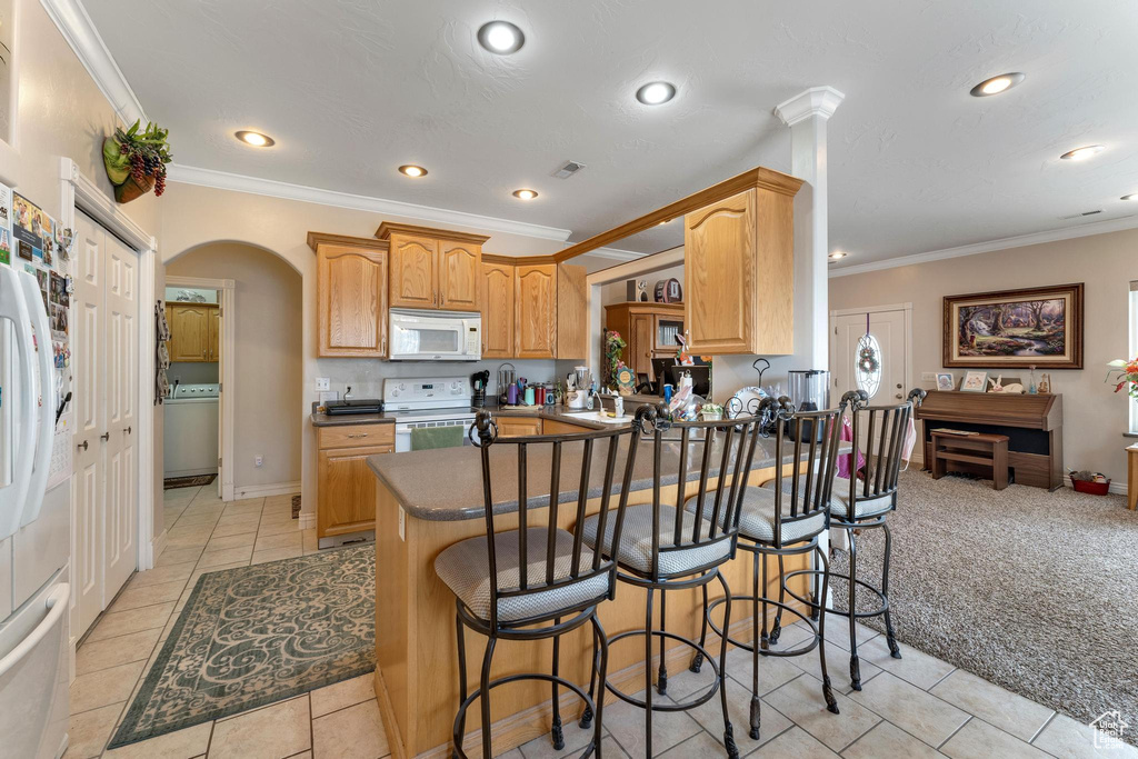 Kitchen featuring light carpet, kitchen peninsula, white appliances, and a kitchen bar
