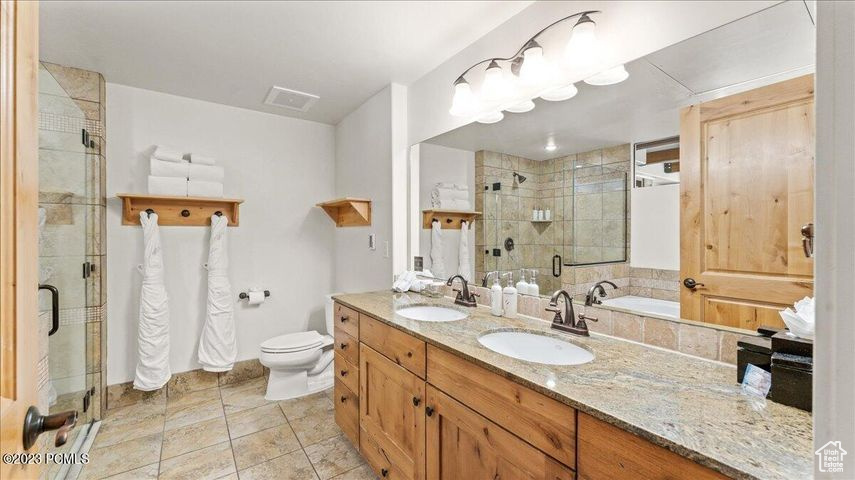 Bathroom with tile floors, double vanity, toilet, and a shower with shower door