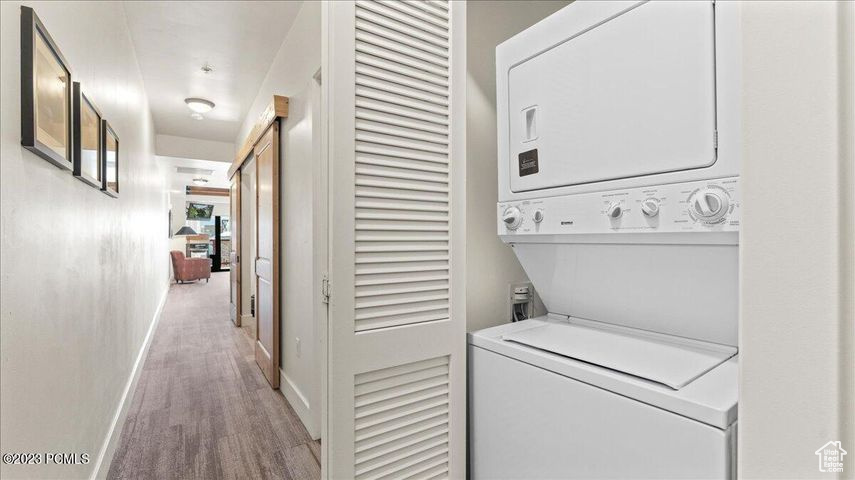 Laundry room with stacked washer / drying machine and light hardwood / wood-style flooring
