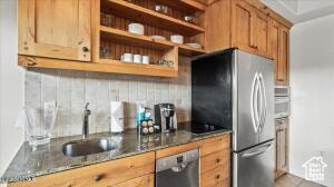 Kitchen with dark stone counters, stainless steel refrigerator, tasteful backsplash, dishwasher, and sink