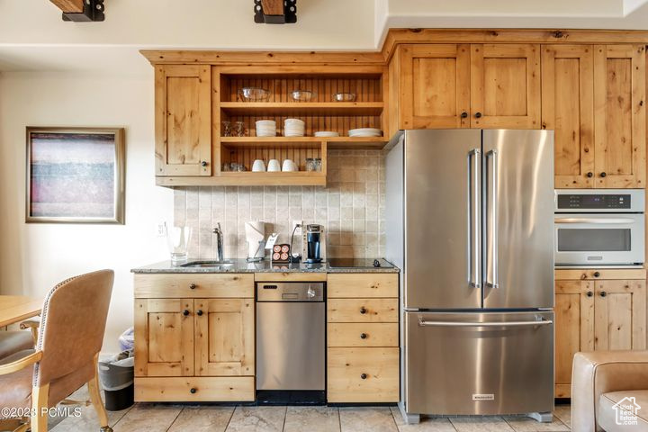 Kitchen featuring dark stone counters, tasteful backsplash, light tile flooring, sink, and stainless steel appliances
