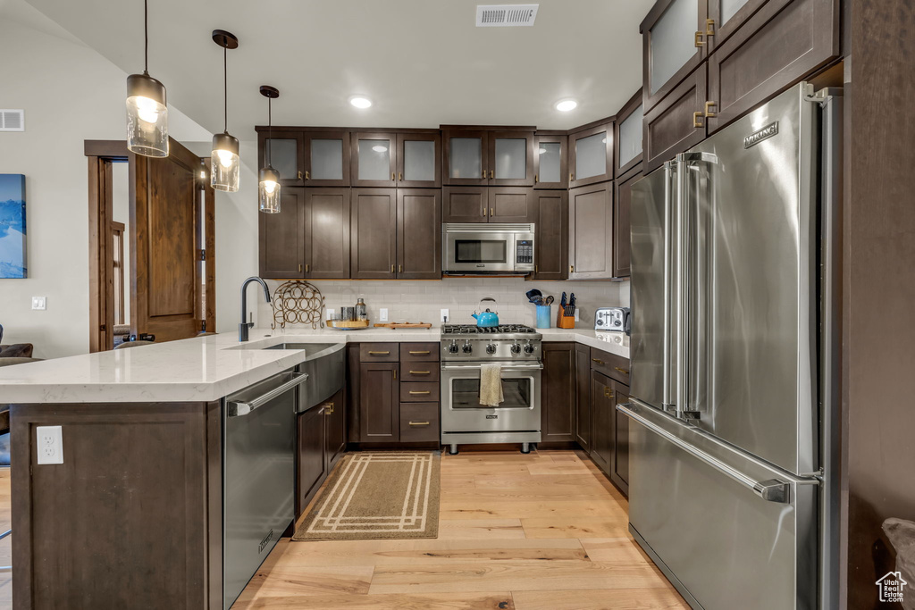 Kitchen with light hardwood / wood-style floors, premium appliances, kitchen peninsula, backsplash, and hanging light fixtures