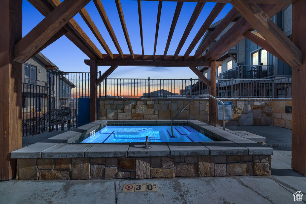Pool at dusk with a pergola, a community hot tub, and a patio area