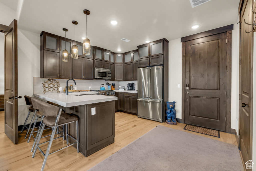 Kitchen featuring dark brown cabinetry, light hardwood / wood-style floors, a kitchen bar, decorative light fixtures, and stainless steel appliances