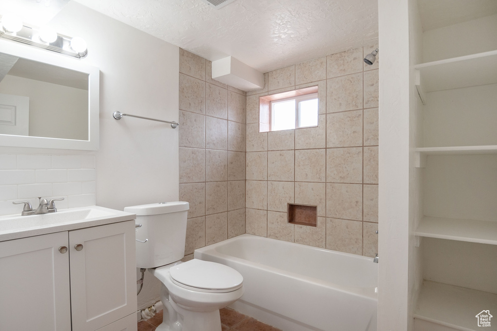 Full bathroom featuring toilet, vanity with extensive cabinet space, tile flooring, tiled shower / bath combo, and a textured ceiling