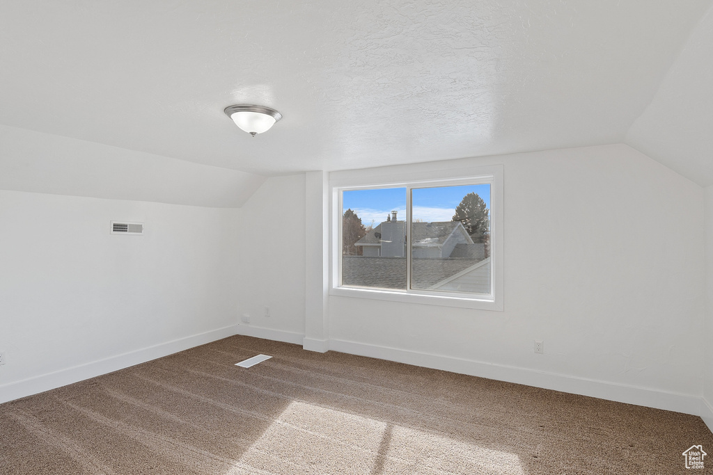 Additional living space with vaulted ceiling, carpet flooring, and a textured ceiling