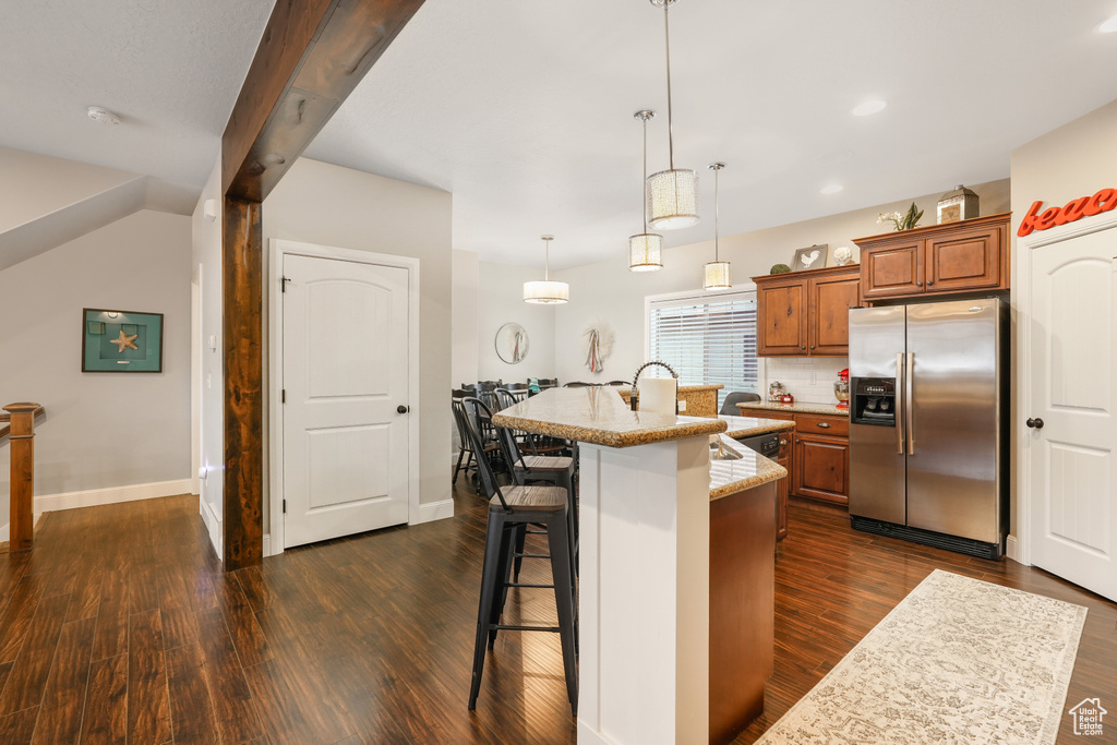 Kitchen featuring a breakfast bar, stainless steel refrigerator with ice dispenser, hanging light fixtures, dark hardwood / wood-style floors, and an island with sink