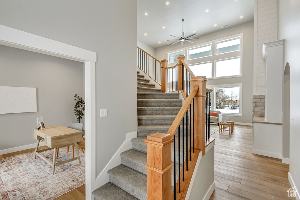 Stairway featuring light hardwood / wood-style flooring, a towering ceiling, and ceiling fan