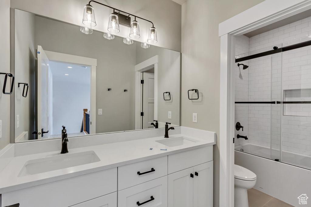Full bathroom with bath / shower combo with glass door, toilet, dual vanity, and tile floors