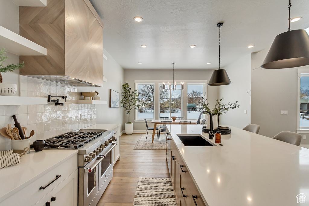 Kitchen featuring pendant lighting, light hardwood / wood-style flooring, sink, tasteful backsplash, and double oven range