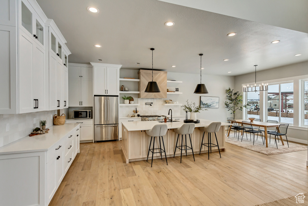 Kitchen featuring tasteful backsplash, white cabinets, a kitchen island with sink, and appliances with stainless steel finishes