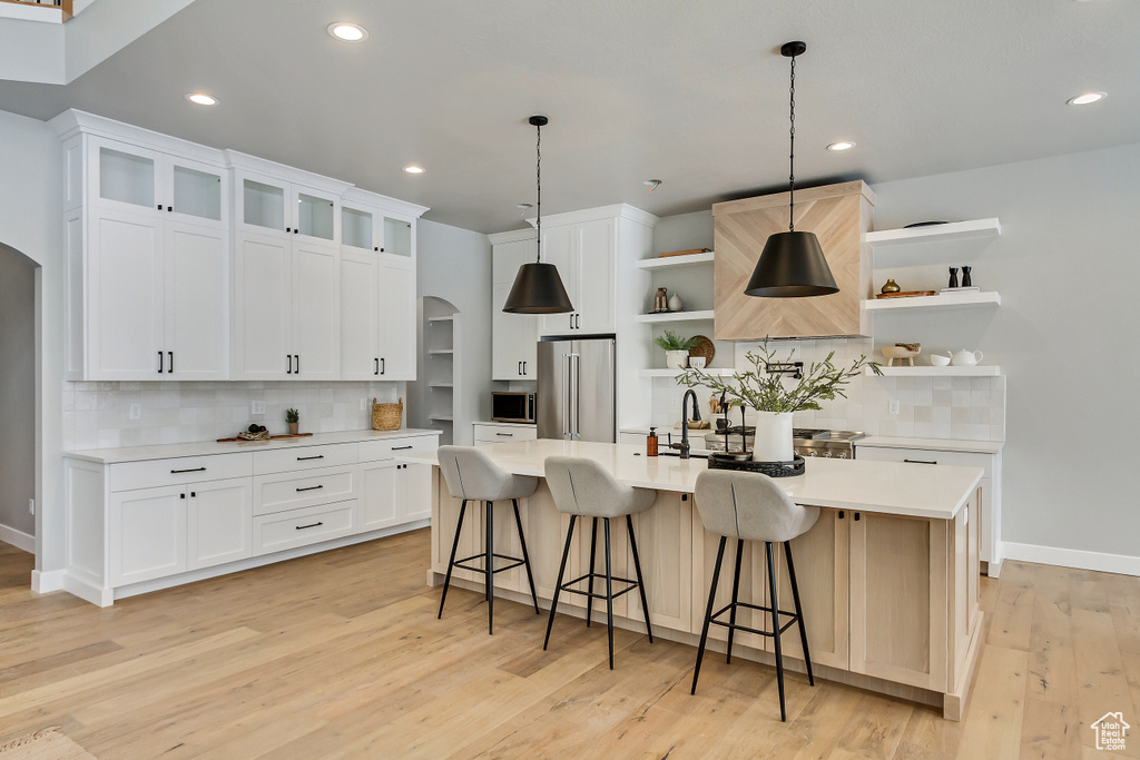 Kitchen with hanging light fixtures, stainless steel appliances, backsplash, light wood-type flooring, and white cabinetry