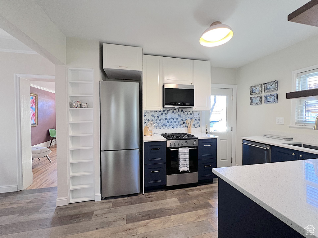 Kitchen featuring stainless steel appliances, white cabinetry, tasteful backsplash, light hardwood / wood-style flooring, and sink
