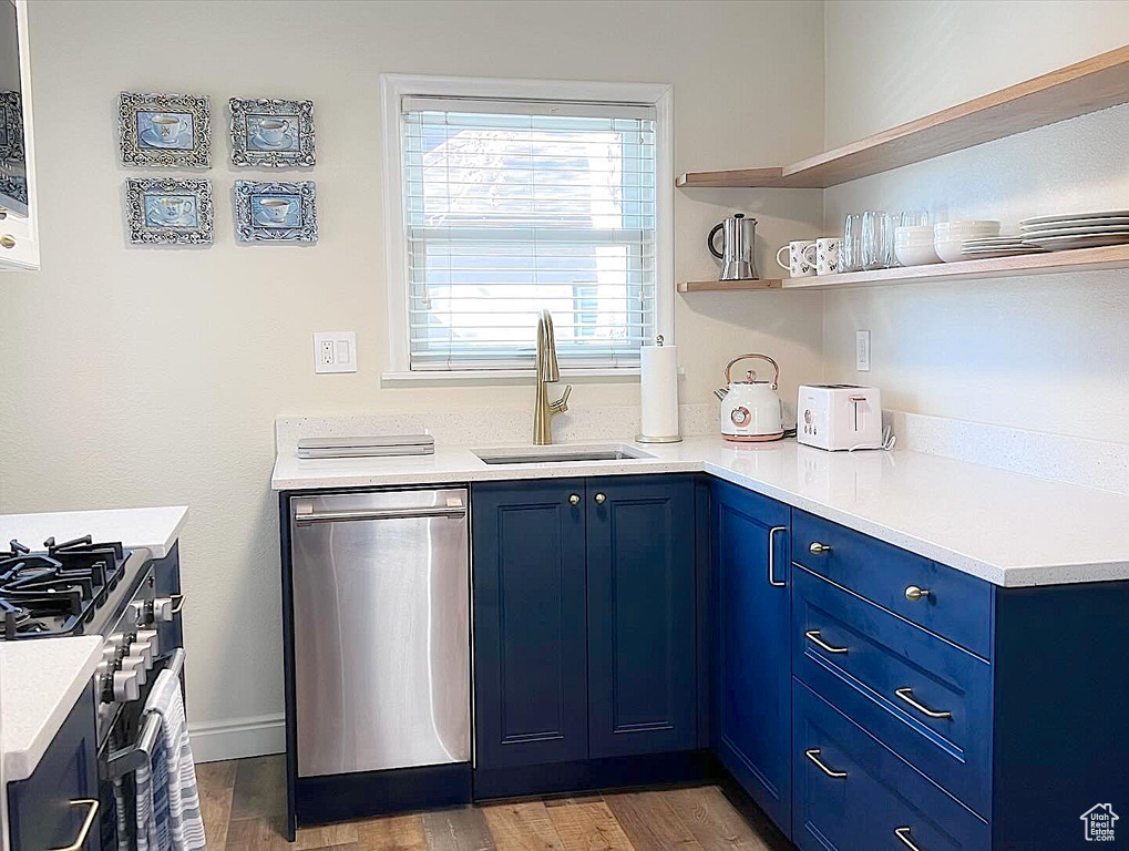 Kitchen featuring dark wood-type flooring, range with gas stovetop, blue cabinets, sink, and dishwasher