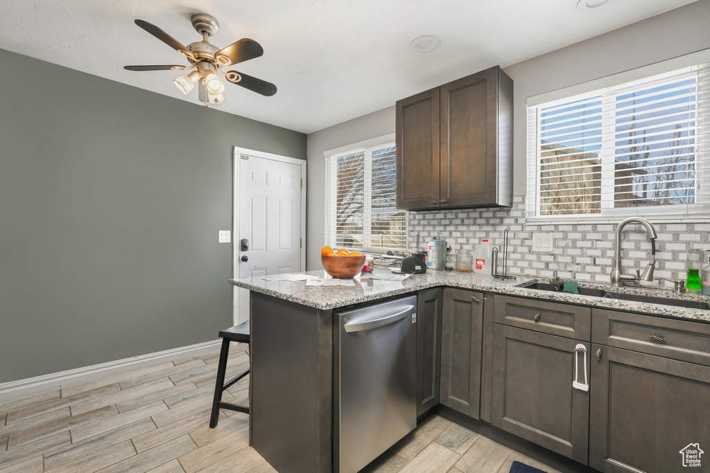 Kitchen featuring light stone countertops, ceiling fan, stainless steel dishwasher, backsplash, and sink