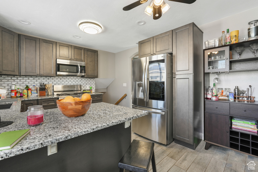 Kitchen featuring light stone countertops, a kitchen bar, appliances with stainless steel finishes, ceiling fan, and backsplash