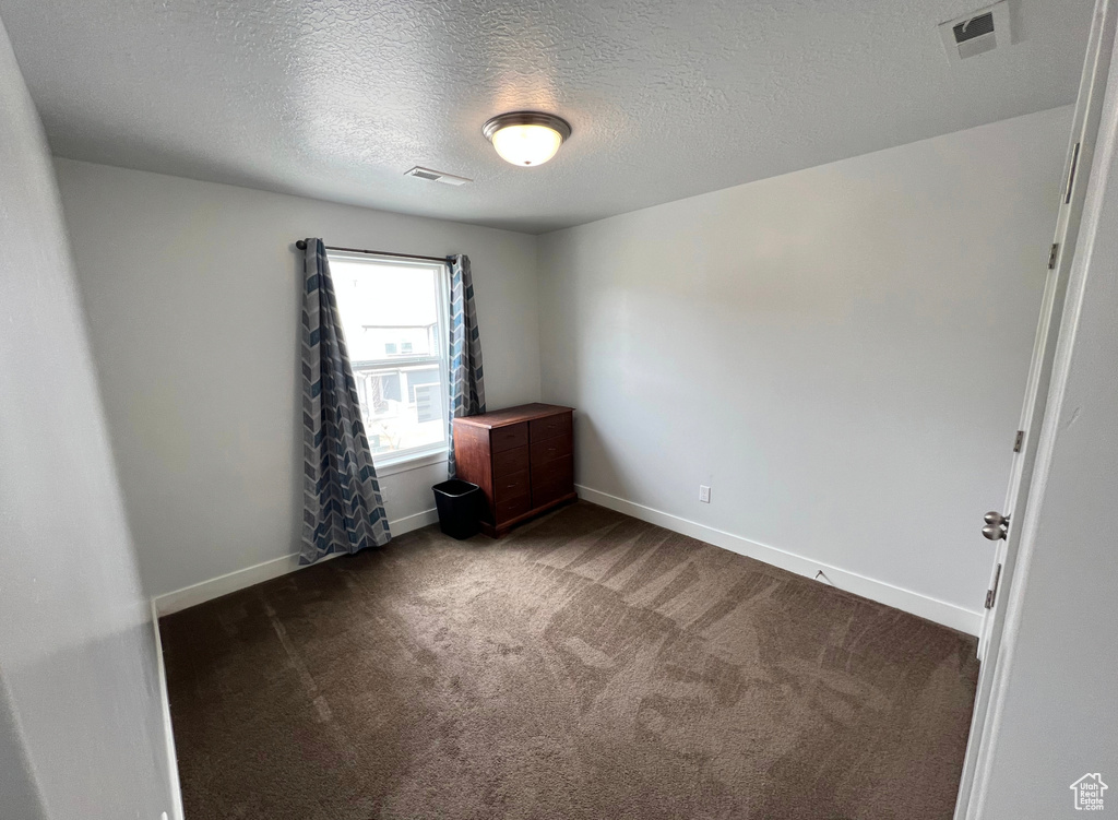Unfurnished room with dark carpet and a textured ceiling