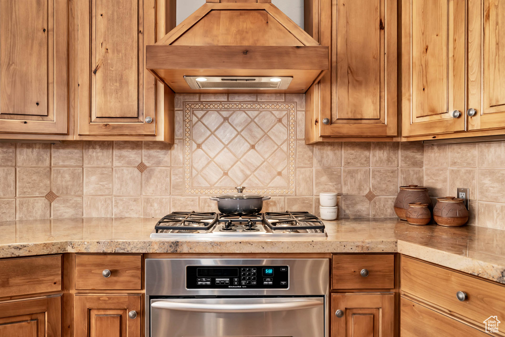 Kitchen featuring premium range hood, appliances with stainless steel finishes, light stone counters, and backsplash