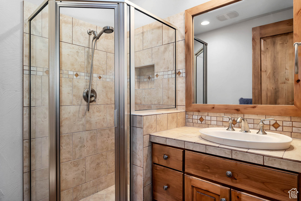 Bathroom featuring a shower with shower door, tasteful backsplash, and oversized vanity