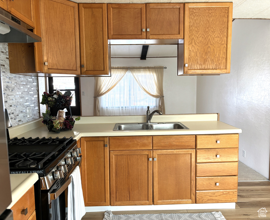 Kitchen featuring backsplash, gas stove, hardwood / wood-style floors, and sink