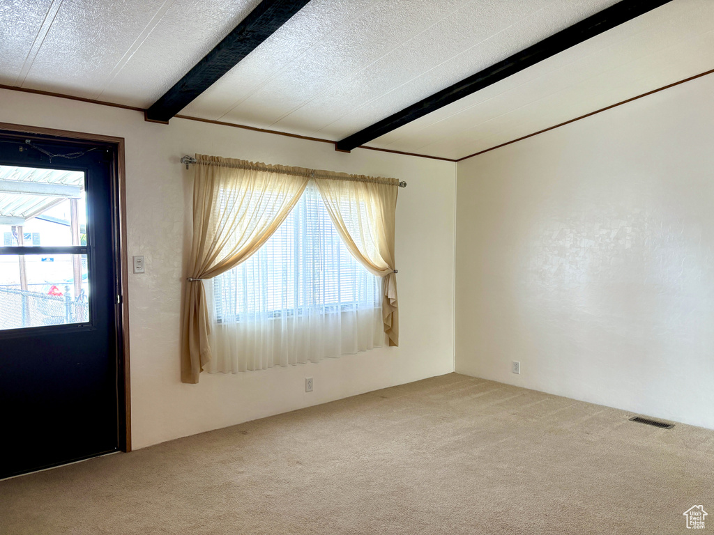 Carpeted empty room featuring beamed ceiling and a textured ceiling