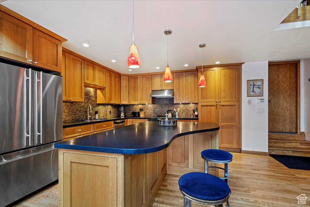 Kitchen with a kitchen island, a breakfast bar area, appliances with stainless steel finishes, backsplash, and light hardwood / wood-style flooring