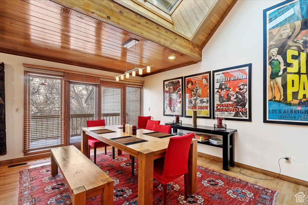 Dining area with light hardwood / wood-style floors, wood ceiling, vaulted ceiling with skylight, and track lighting