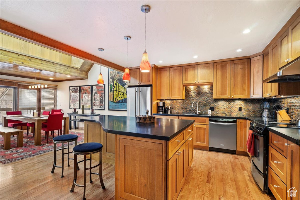 Kitchen featuring light hardwood / wood-style floors, appliances with stainless steel finishes, decorative light fixtures, and a center island