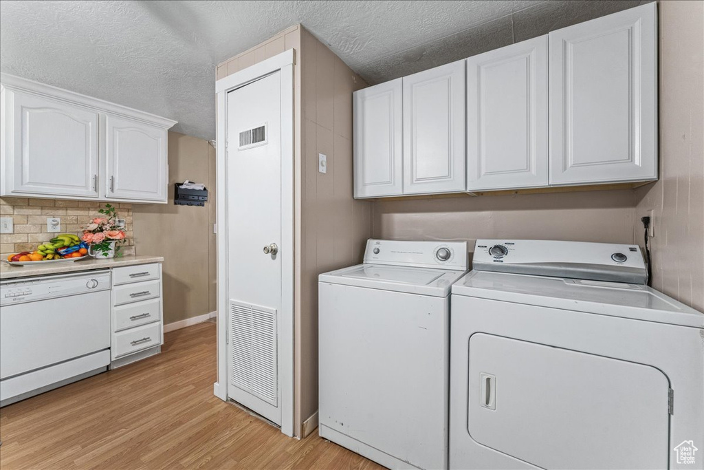 Washroom with washing machine and clothes dryer, light hardwood / wood-style floors, and a textured ceiling