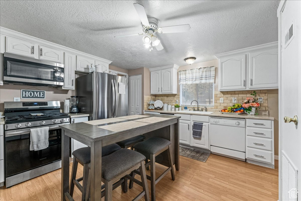 Kitchen featuring backsplash, light wood-type flooring, appliances with stainless steel finishes, and ceiling fan