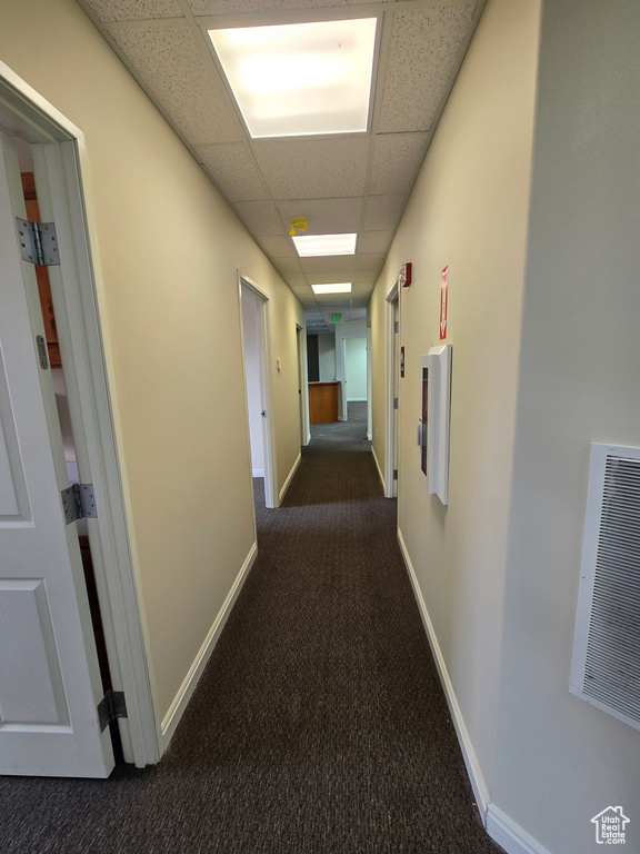 Hallway featuring a drop ceiling and dark carpet