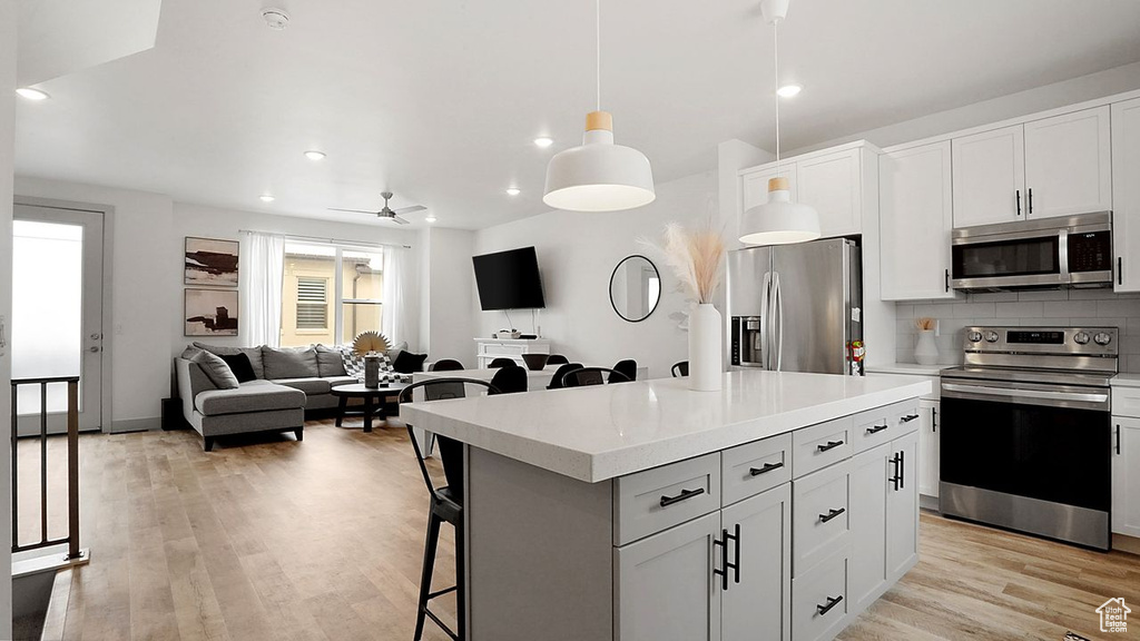 Kitchen with a breakfast bar, a center island, stainless steel appliances, ceiling fan, and light wood-type flooring