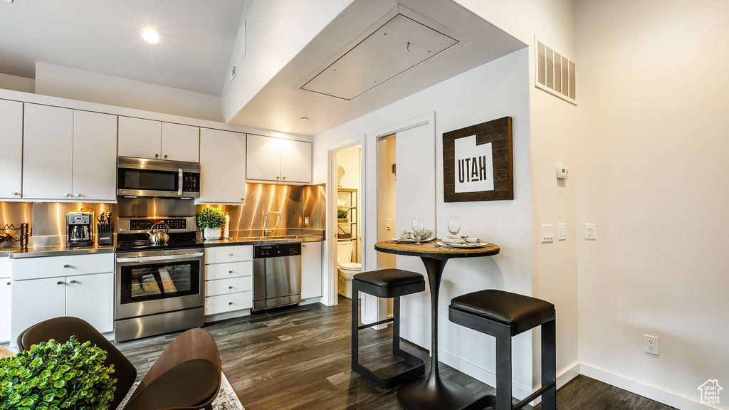 Kitchen featuring stainless steel appliances, white cabinets, stainless steel counters, and backsplash