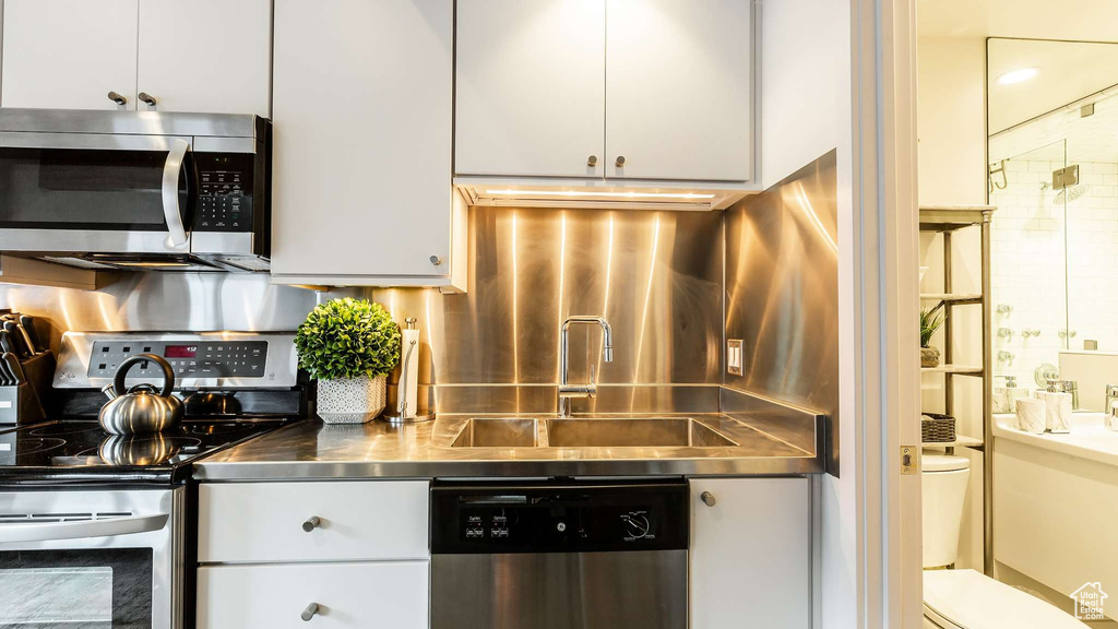 Kitchen featuring appliances with stainless steel finishes, stainless steel counters, sink, tasteful backsplash, and white cabinetry