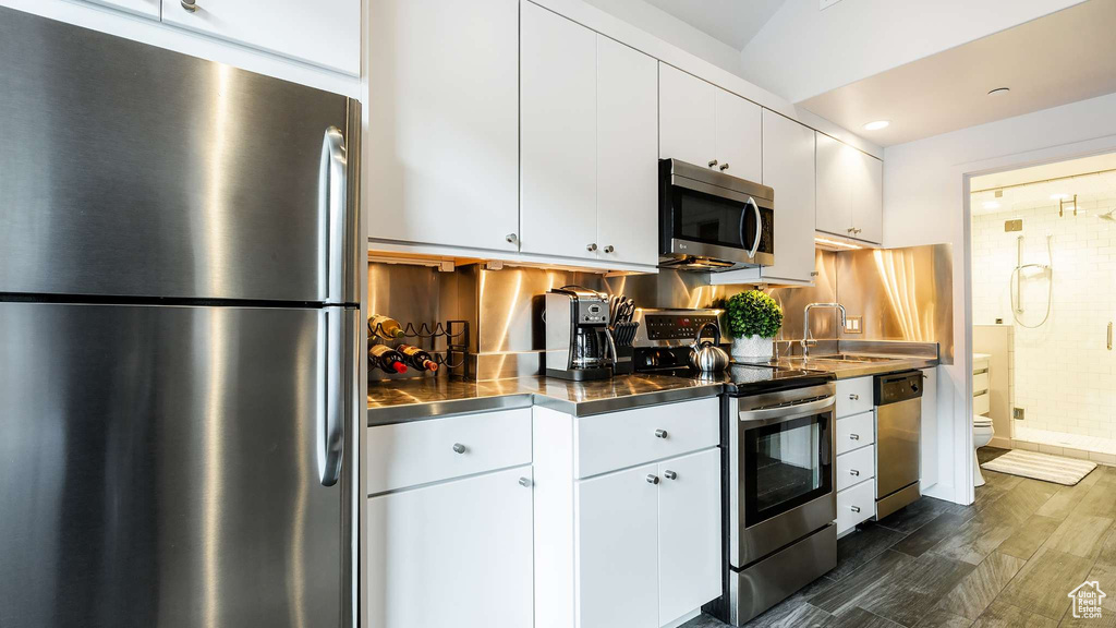 Kitchen featuring stainless steel counters, appliances with stainless steel finishes, dark wood-type flooring, and white cabinetry