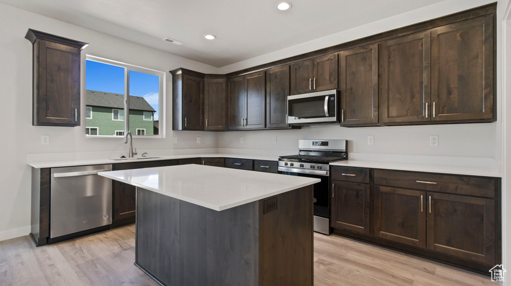 Kitchen with light wood-type flooring, appliances with stainless steel finishes, a kitchen island, and dark brown cabinets