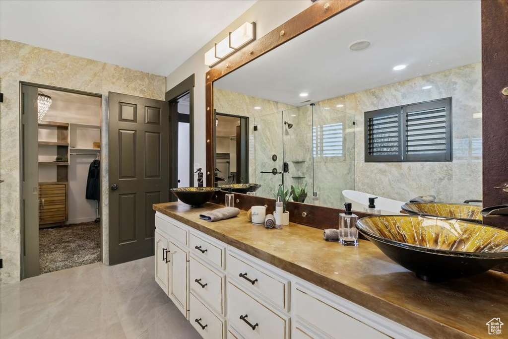 Bathroom with oversized vanity, dual sinks, shower with separate bathtub, tile floors, and tile walls
