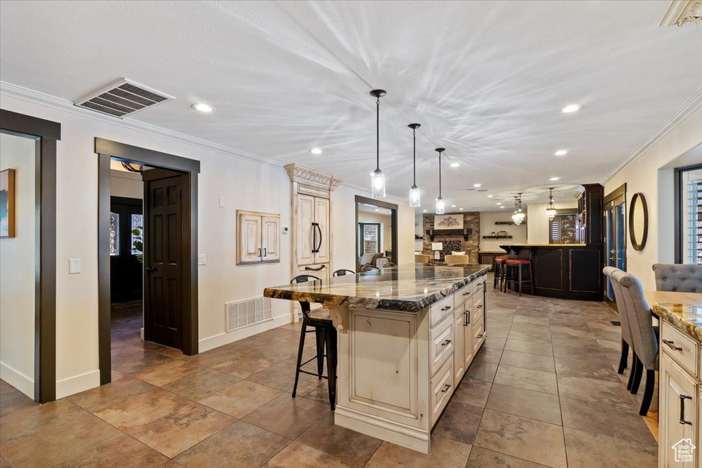 Kitchen featuring crown molding, a breakfast bar, pendant lighting, an island with sink, and light tile floors