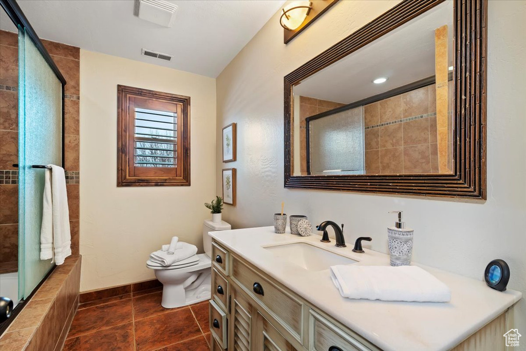 Full bathroom featuring tile floors, shower / bath combination with glass door, toilet, and vanity