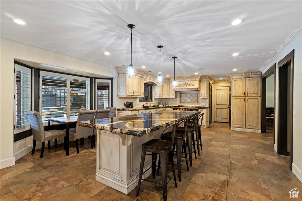 Kitchen featuring a kitchen bar, pendant lighting, a center island, ornamental molding, and tile floors